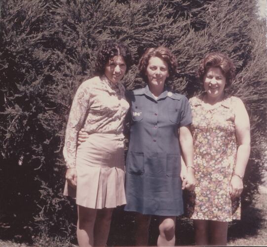 Three women in front of hedge.