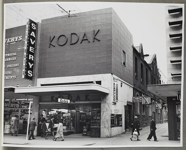 Street view of shopfronts, one with Kodak signage.