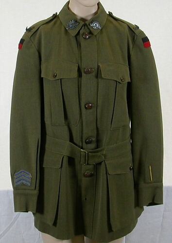 Khaki woollen tunic. Two hip pockets with button flaps. Two breast pockets with pleat flaps. Buckle waistband.