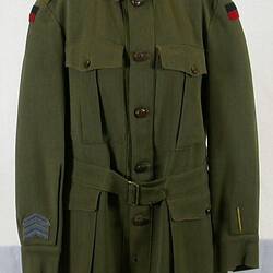 Khaki woollen tunic. Two hip pockets with button flaps. Two breast pockets with pleat flaps. Buckle waistband.