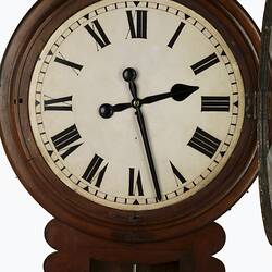 Detail wall clock with cedar drop dial case. White clock face with black Roman numerals and hands. Open glass.