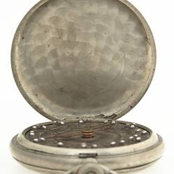 Silver metal round fob watch sitting within metal cover open to show inner lid.