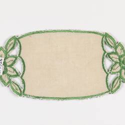 Back of rectangular cream doily with rounded ends that feature a flower motif with green worked edging.