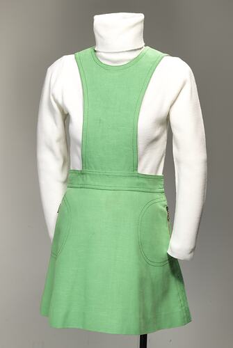 Lime green linen mini pinafore dress with zippered pockets on sides of skirt.