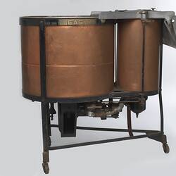 Washing machine with one large copper barrel and one smaller one connected at the base by a metal frame.