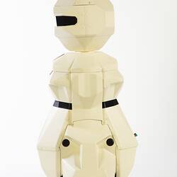 Side view of cream plastic robot with angular human-like shape, ie. head, shoulders, waist and legs. Black plastic features.
