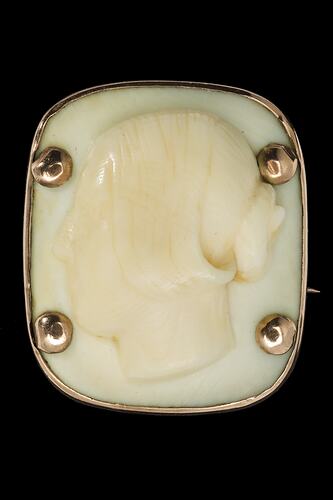 Square cameo with rounded corners featuring a white female bust facing left, hair up in a bun. Four prominent corner gold pins secure the cameo to its gold setting.