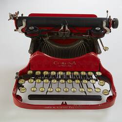 Red metal typewriter with 32 keys, black plastic spacebar at front, black roller for paper at top back. Front