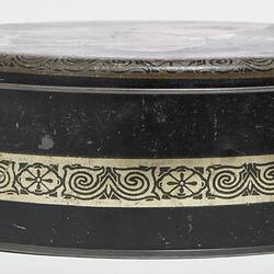 Side view of round black metal tin with lid. Central decorative gold band.