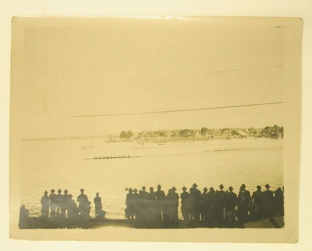 Row of men watching boat race.