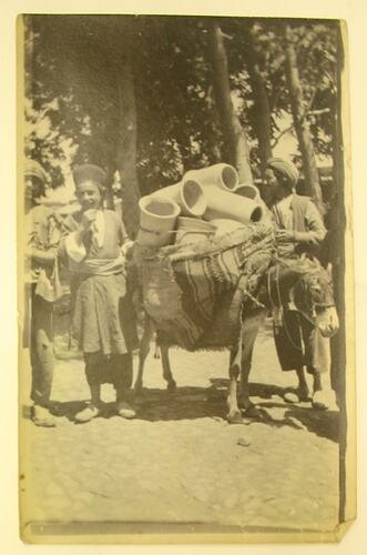 Donkey carrying pots and three young men.
