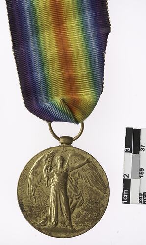 Round medal showing woman with wings holding plant leaf, with rainbow coloured ribbon.