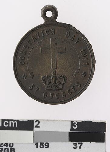 Round bronze coloured medal with cross above crown and text surrounding.