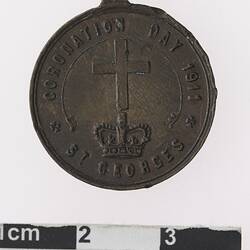 Round bronze coloured medal with cross above crown and text surrounding.