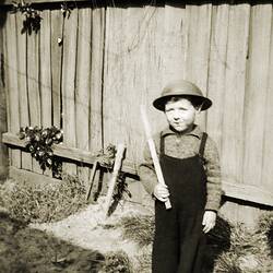 Young boy in army helmet standing to attention in his backyard.