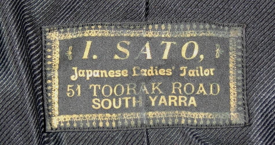 Black clothing label with name and adress of business in gold.