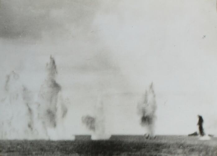 Multiple explosions in the water in background, ocean in foreground.