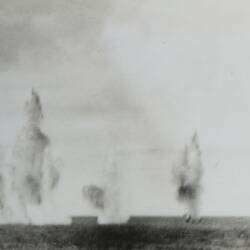 Multiple explosions in the water in background, ocean in foreground.