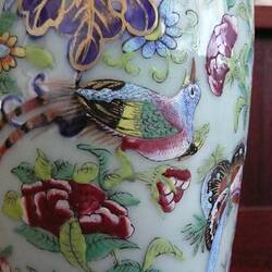 Detail of vase with decorative bird and flower and foliage in blues, reds, gold and greens.