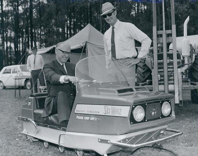 A man sitting in a snowmobile, and other men watching.