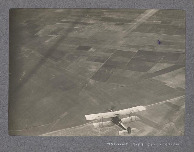 Aerial view of aircraft in flight above cultivated land.