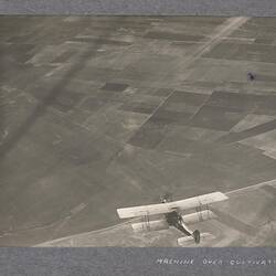 Aerial view of aircraft in flight above cultivated land.