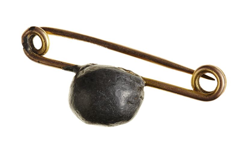 Gold pin brooch with small lead bullet mounted on it.