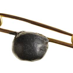 Gold pin brooch with small lead bullet mounted on it.