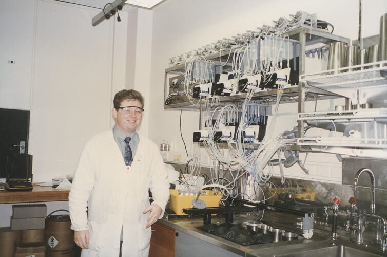 Man in lab coat at work bench, smiling.
