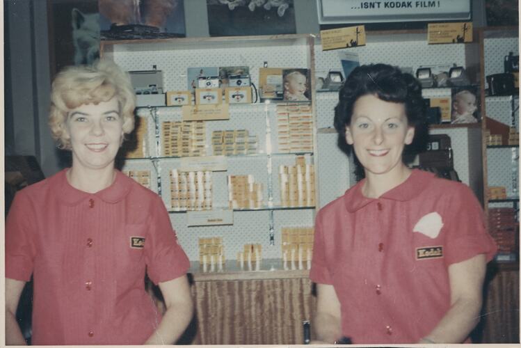 Two uniformed women smiling in photosupply shop.