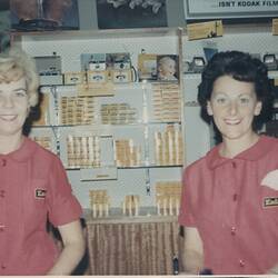 Two uniformed women smiling in photosupply shop.