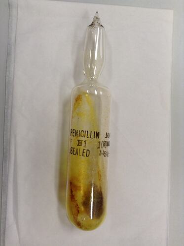 Hand-blown cylindrical glass ampoule. Black text on glass, dried brown compound inside.