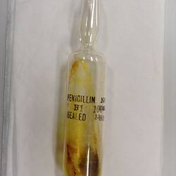 Hand-blown cylindrical glass ampoule. Black text on glass, dried brown compound inside.