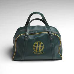 Green school bag with central zipper, two handles, yellow piping and logo on side.