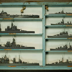 Blue and grey wooden case holding 9 grey ship models in two columns.