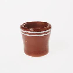 Miniature brown ceramic mug. No handle. Features two white painted lines around rim.