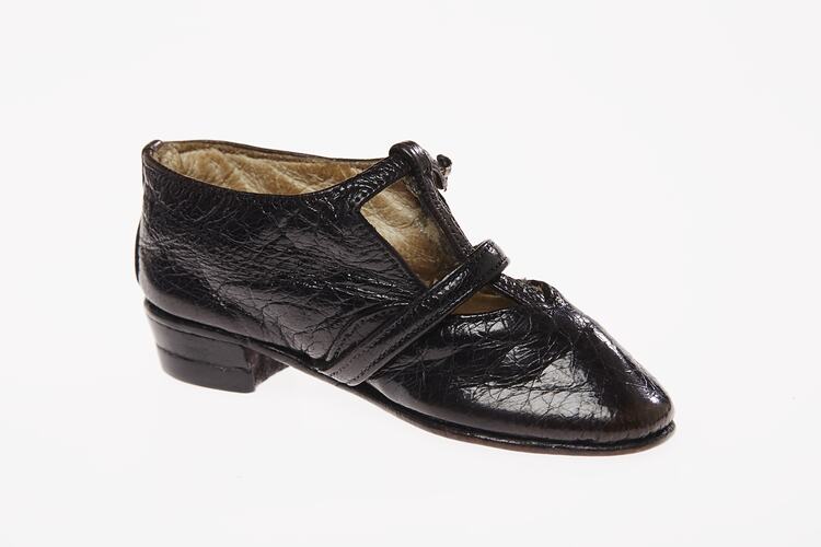 Miniature hand-sewn black leather shoe with strap and glass button fastener.
