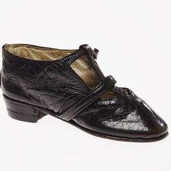 Miniature hand-sewn black leather shoe with strap and glass button fastener.