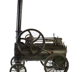 Model of black moveable steam engine on four wheels with tall chimney at front. Left profile.