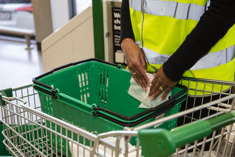 Hands wiping down green shopping basket in trolley.