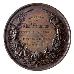 Round medal with engraved text framed by decorative botanical wreath.