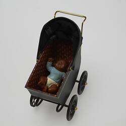 Black metal miniature pram. Maroon lining has gold tulips patterns. Contains baby doll with dark brown hair an