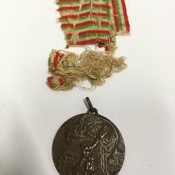 Round dark medal with separate frayed green, red and white striped ribbon.