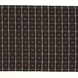 Black woven square fabric with fringe and white grid pattern with red flower in each section.
