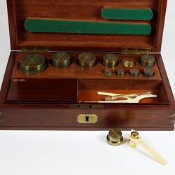 Standard gilt brass weights shown in an open wooden box.