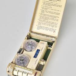 Rectangular cream metal case with four white labelled buttons. Open showing instructions and 2 spools.