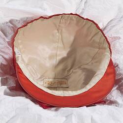 White fabric lining inside of red jockey cap. White label, yellow lettering.