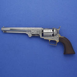 A navy percussion revolver on a blue background, with a black handle and silver trigger.