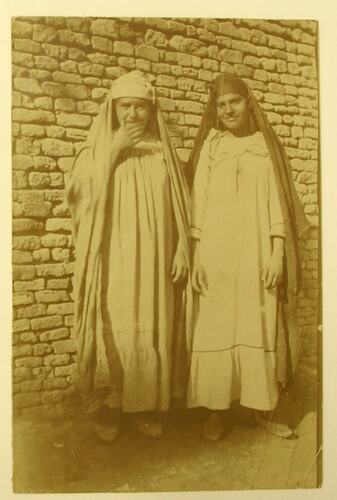 Two women wearing long dresses and head coverings.