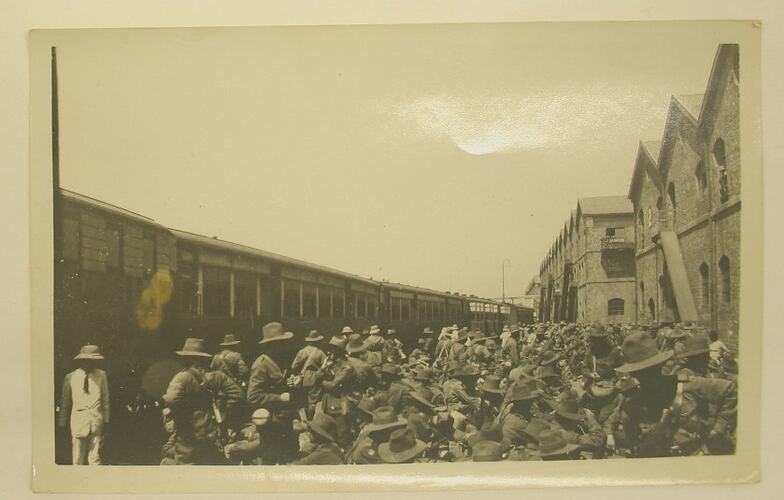 Crowd of men in military uniform, gathered on a train platform.